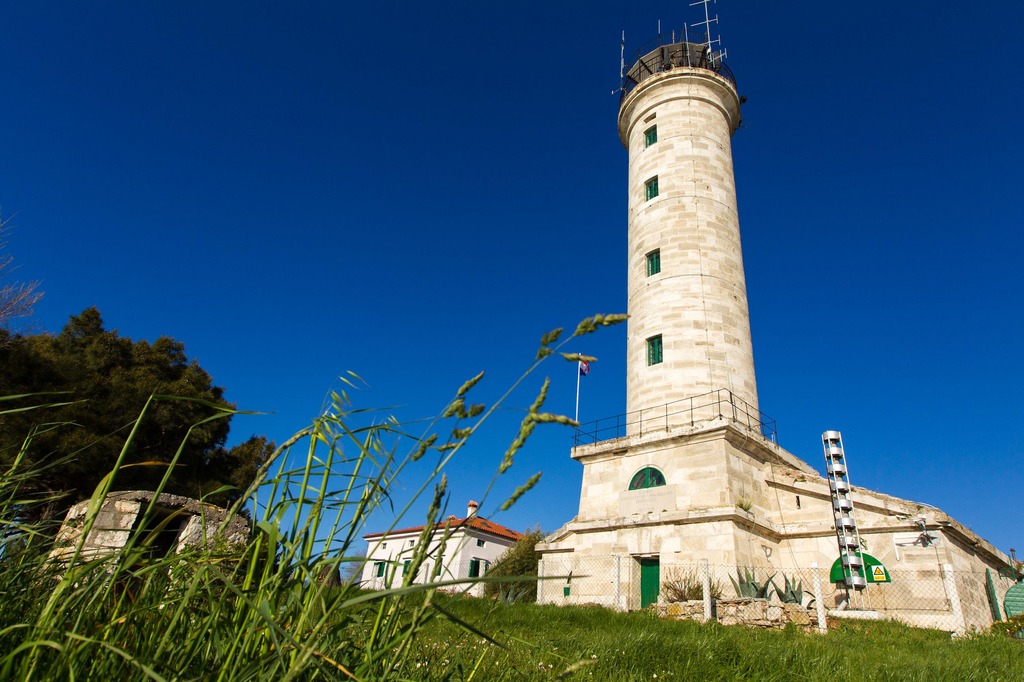 A stone lighthouse shown in the distance against a backdrop of a deep blue sky.