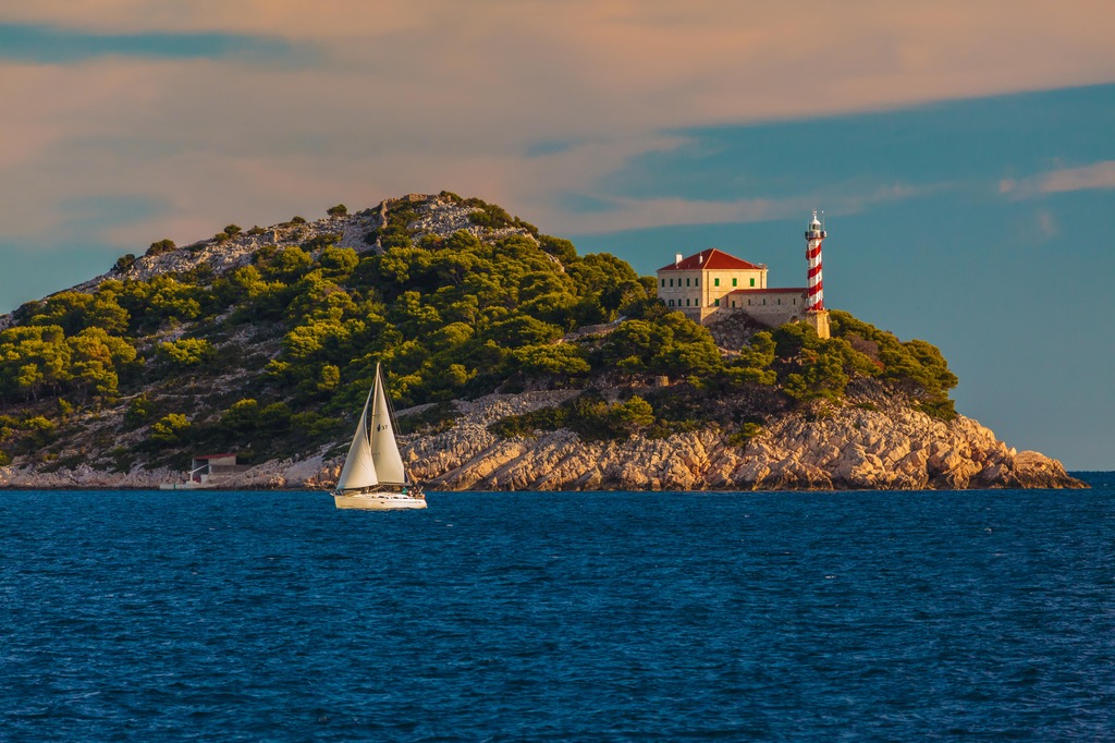 Island in the distance with a lighthouse tower (white and red stripes) on the right side of it. Sea is shown in the foreground and a sailboat sailing close to the island.